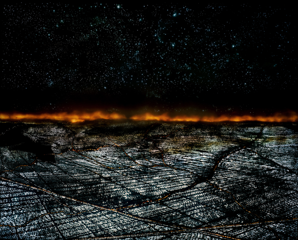 Una città vista dall'alto, di notte, con un incendio all'orizzonte.